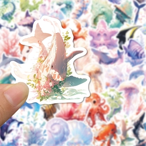 Close-up of a hand holding a watercolor whale and flower sticker for decoration