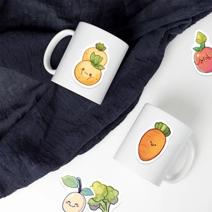 Close-up of ceramic mugs and cute cartoon vegetable stickers on textured blue fabric