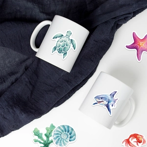 Close-up of watercolor sea creature stickers on a white ceramic mug with starfish and turtle