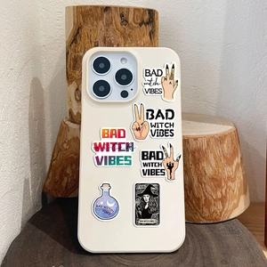 Detail showing Bad Witch Vibes stickers on a cream phone case with vintage art