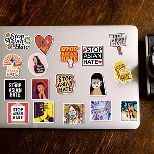 Macro detail of Stop Asian Hate stickers with artistic illustrations on laptop cover