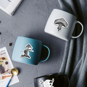 Black and white gothic mushroom stickers displayed on mugs in a minimalist lifestyle setting