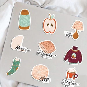 Detail of cozy autumn stickers with warm sweater and hot cocoa on laptop surface