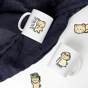Close-up of white ceramic mugs featuring cute brown bear stickers and cartoon illustrations