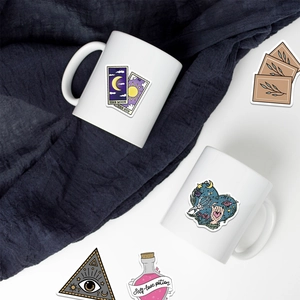 Close-up of tarot mugs and waterproof bohemian witch stickers on blue fabric background