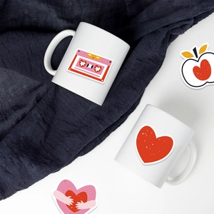 Détail des autocollants cœur et cassette rose sur des tasses en céramique blanche