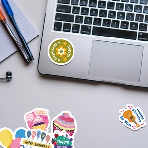 Close-up of waterproof birthday stickers on a laptop featuring cupcakes and balloons