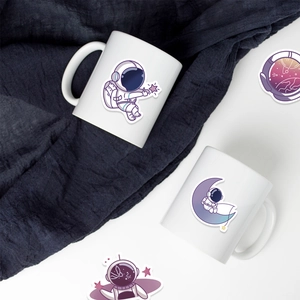 Detail of white ceramic astronaut mugs with cute outer space stickers on fabric background