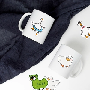 Close-up of cute cartoon white goose waterproof stickers on ceramic mugs and blue fabric