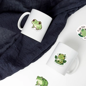 Close-up of ceramic mugs decorated with cute green frog stickers and creative cutouts