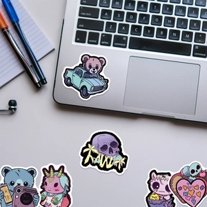 Close-up of cute gothic stickers including purple skull and pink bear on silver laptop