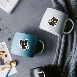 Detailed view of matte ceramic mugs with cute black cat stickers in minimalist urban setting