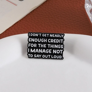 Minimalist black enamel rectangle brooch with white lettering on a white porcelain dish