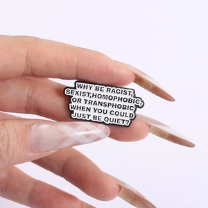 Detail of hand holding a black enamel brooch with white anti-discrimination text statement