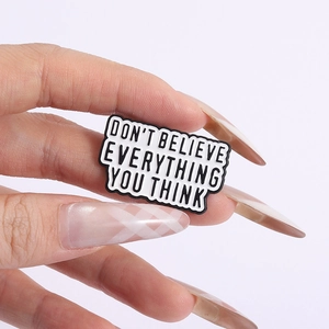 Detail shot of hand holding enamel pin with text Don't Believe Everything You Think