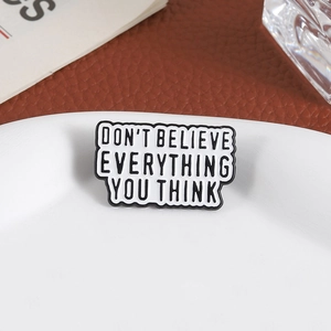 Creative enamel pin with 'DON'T BELIEVE EVERYTHING YOU THINK' quote on white dish