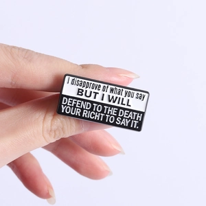 Detailed close-up of a rectangular enamel pin featuring black and white quote lettering