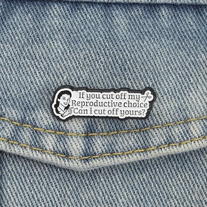 Creative feminist enamel pin on blue denim jacket with black and white retro design
