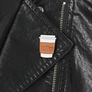 Close-up of enamel coffee cup brooch with coffee text pinned on a black leather lapel