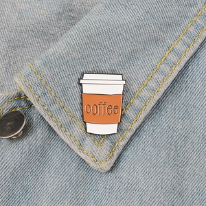 Cartoon enamel coffee cup brooch pin with brown and white lettering on denim jacket
