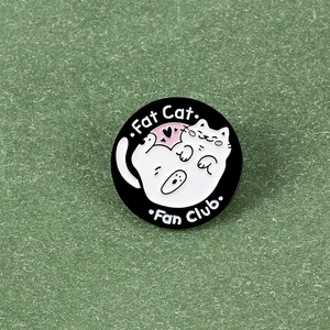 Detail of a round black enamel pin featuring a cute white fat cat and Fan Club text