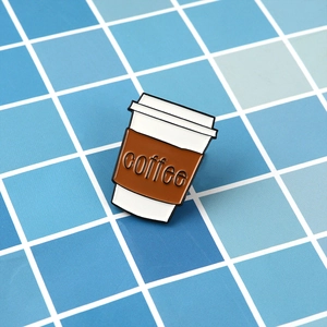 Close-up of enamel coffee cup pin with embossed coffee text on blue tile background