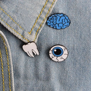 Set di spille in smalto con disegni di cervello, dente e occhio su denim blu