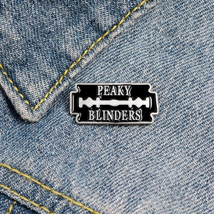 Détail du badge Peaky Blinders en forme de lame de rasoir sur une veste en jean bleu