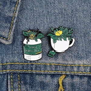 Lot de deux broches en émail avec fleurs jaunes dans flacons et tasses sur veste en jean
