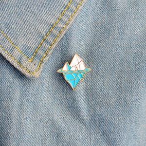 Fashionable iceberg enamel pin with blue wave design pinned on denim fabric