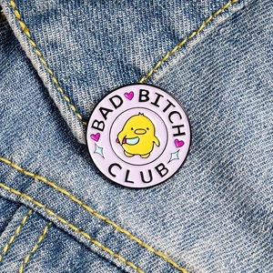 Bad Bitch Club cartoon duck enamel pin with dagger on blue denim jacket fabric