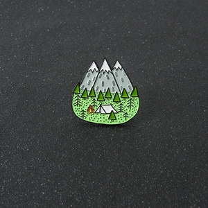 Détail d'un badge en émail avec montagnes enneigées, pins et feu de camp sur fond noir