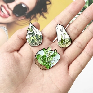 Detailed view of three cactus terrarium enamel pins held in hand to show actual size