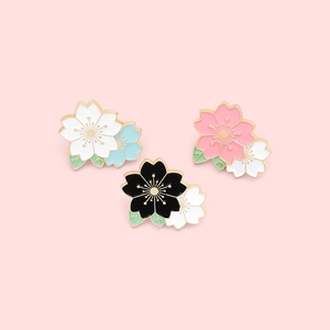 Macro shot of three floral cherry blossom enamel brooches in various colors on pink background