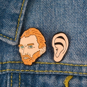 Artistic Van Gogh portrait and ear enamel pins attached to blue denim jacket fabric