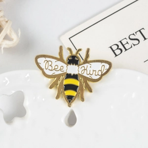 Detailed macro of a Bee Kind enamel brooch featuring yellow and black stripes