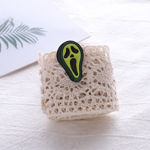 Close-up of green scream mask enamel pin on lace roll for accessory size comparison
