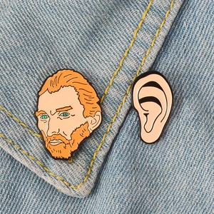 Detailed view of Van Gogh portrait and ear enamel pins on blue denim fabric