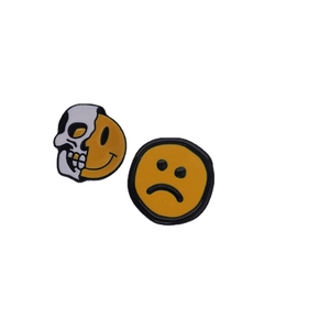 Creative enamel pins featuring a smiling skull face and a yellow sad expression badge