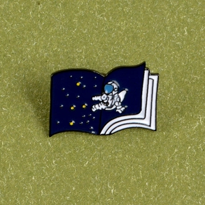 Creative astronaut floating in space book enamel pin with a dark blue starry sky design