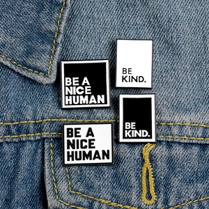 Set of 4 enamel pins with Be A Nice Human and Be Kind slogans on denim jacket