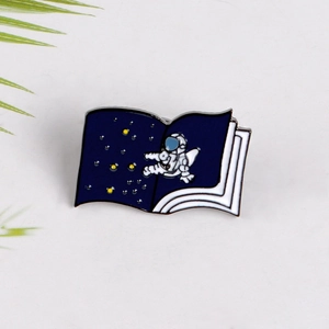 Detail shot of an astronaut enamel pin on an open starry book with blue background