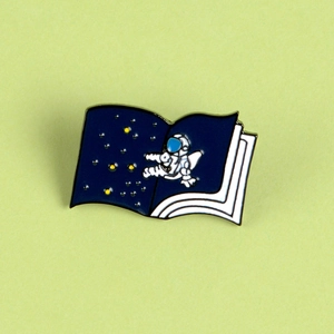 Detailed macro view of an astronaut enamel pin on an open book with starry sky background