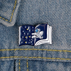 Detail of an enamel astronaut pin on an open book over a denim jacket background