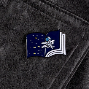 Detail of creative astronaut book enamel pin on textured black leather surface