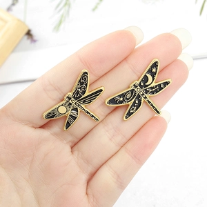 Dragonfly pins with sun and moon enamel patterns held by hand for scale display