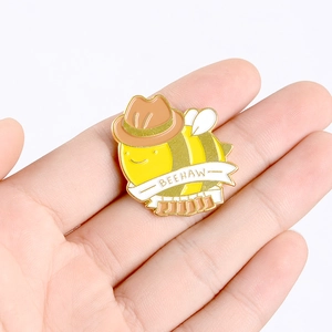 Détail d'une broche abeille avec chapeau de cowboy, bottes et texte Beehaw tenue en main
