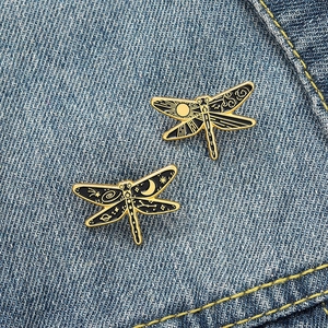 Detailed view of dragonfly enamel pins with celestial gold sun and moon patterns on denim