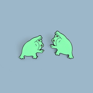 Gros plan de deux épinglettes en émail grenouille verte aux poses amusantes