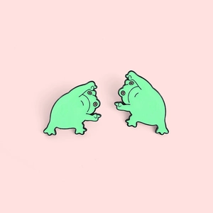 Détail de deux épinglettes en émail grenouille verte rigolotes sur fond rose tendre